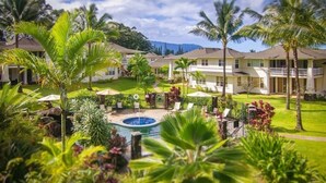 Un resort con varias edificaciones de dos pisos, piscina y exuberante vegetación tropical.