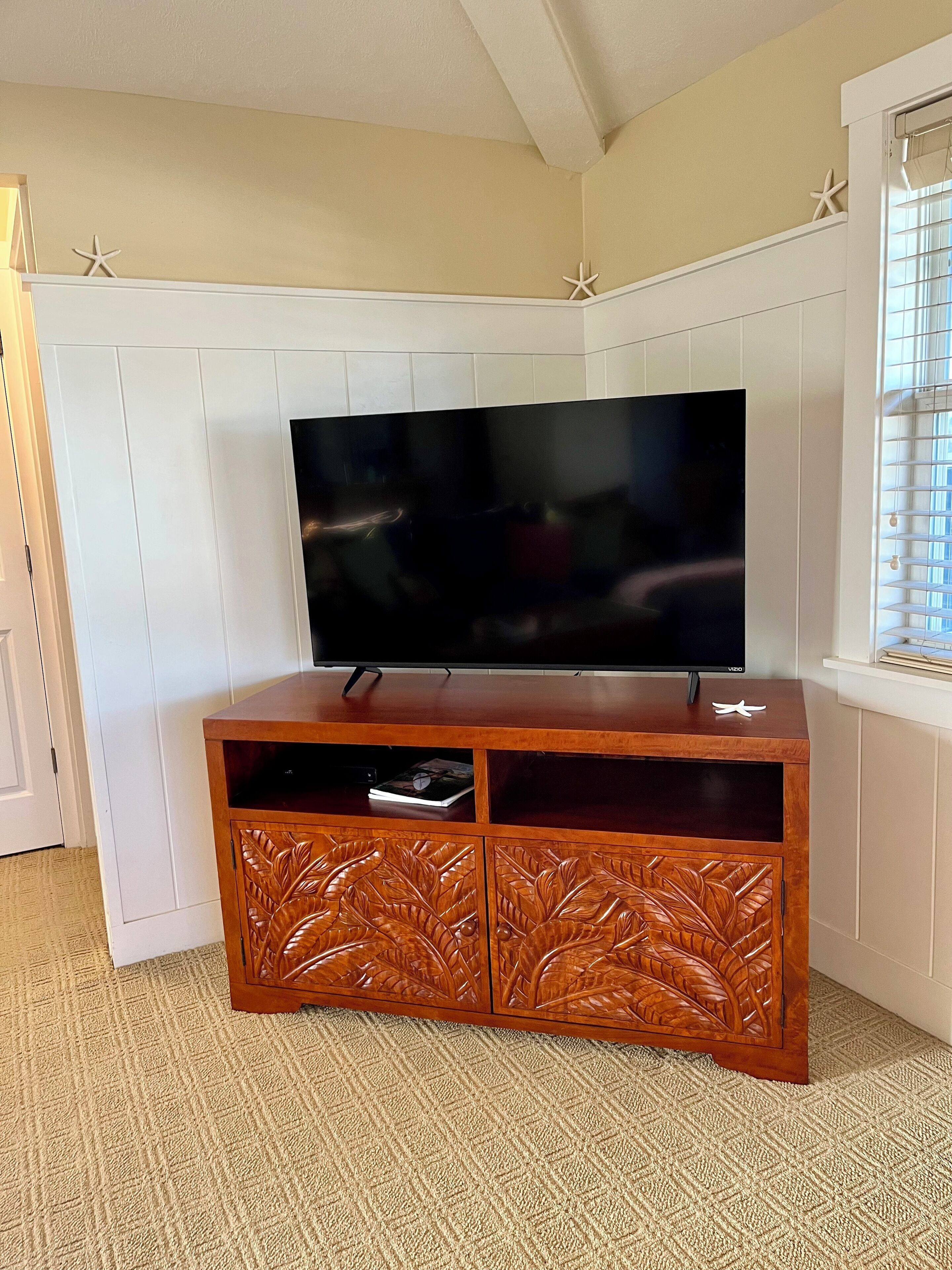 A flat-screen TV on a wooden entertainment unit with leaf-carved details, positioned against a white paneled wall with starfish decorations.