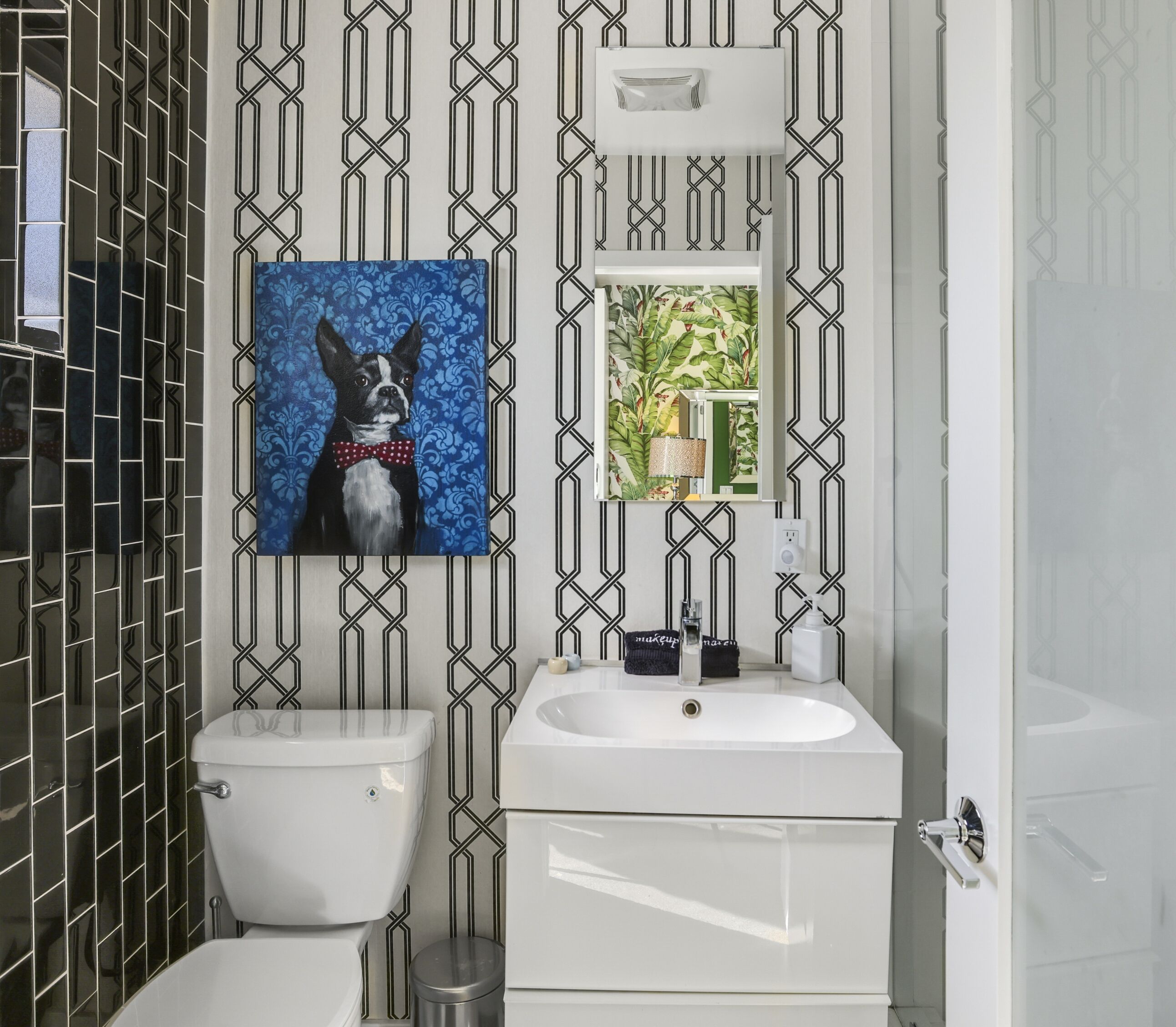 A bathroom with a toilet, sink, and mirror. There is a framed picture of a dog on the wall.