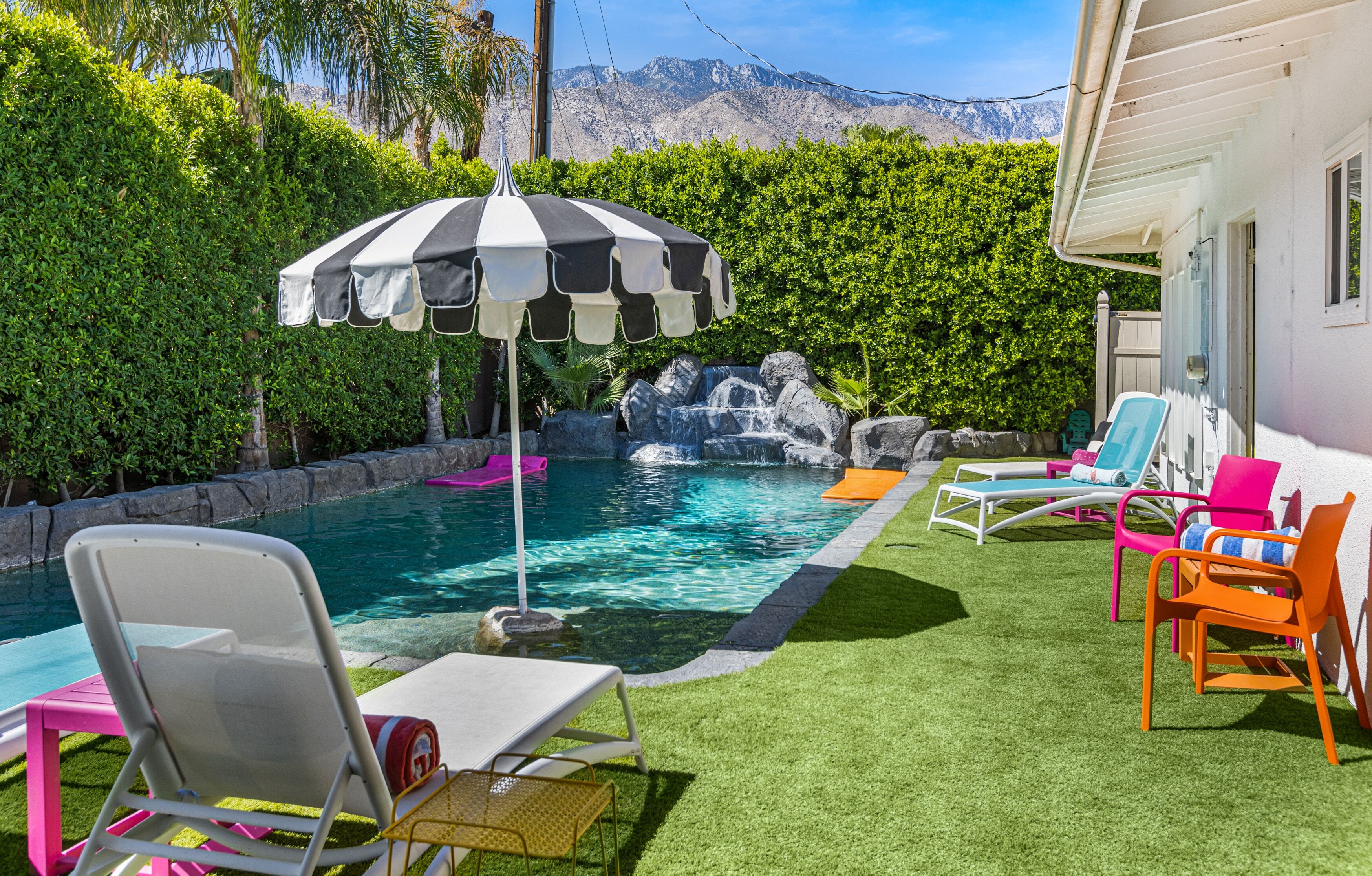 A backyard with a swimming pool, a waterfall feature, and colorful lounge chairs.