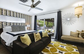 Ein Schlafzimmer mit Bett, einer Sitzecke, einem Deckenventilator, einer Kronleuchter und Blick durch eine Glastür.