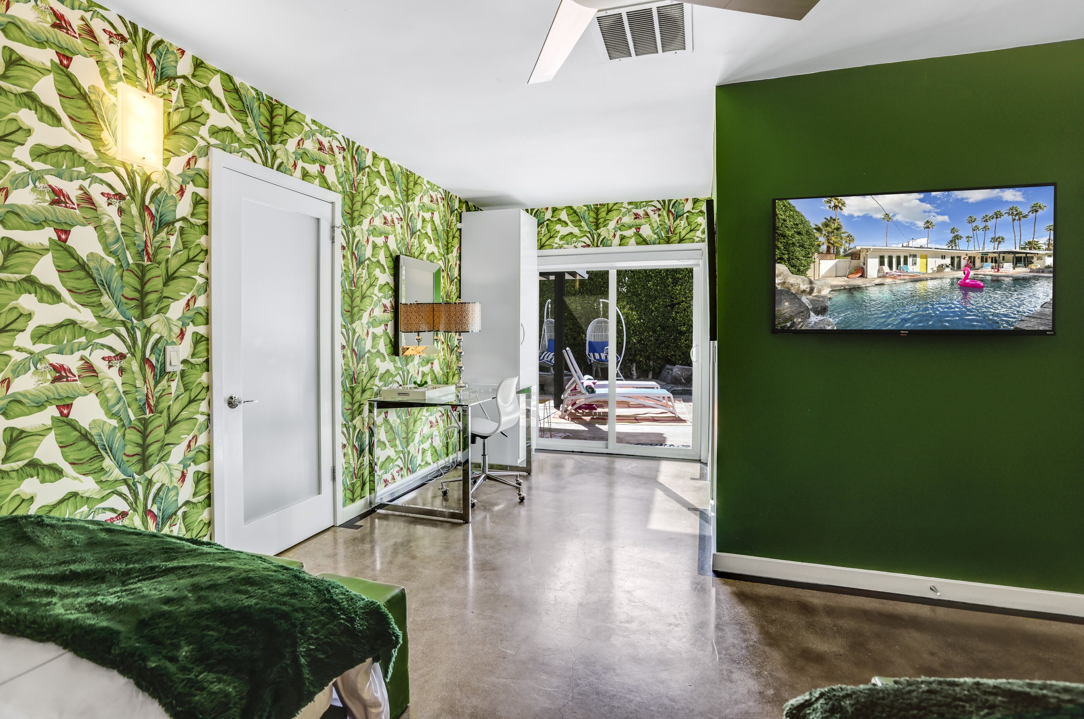 Una habitación con una pared verde, un televisor que muestra una piscina y una puerta que da a un balcón con vistas a la piscina.