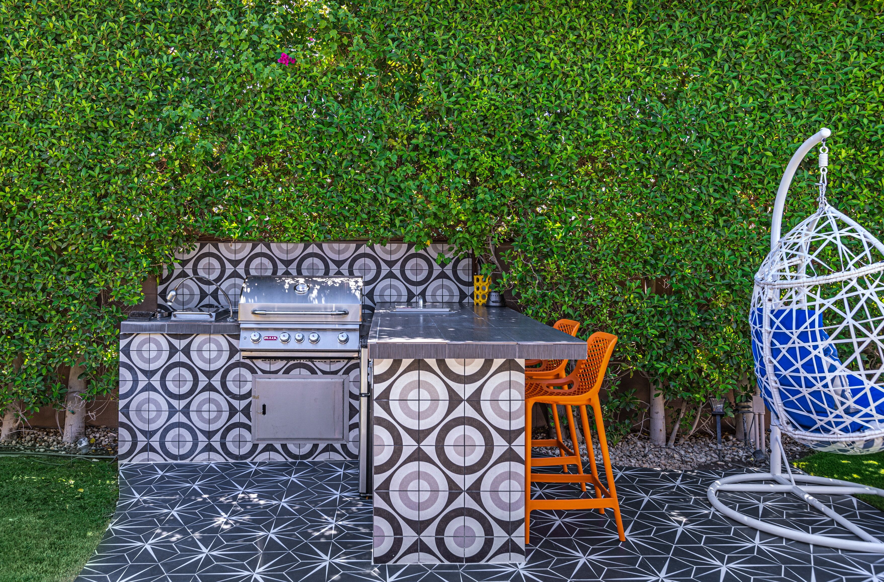 An outdoor kitchen with a grill, a table, and orange chairs.