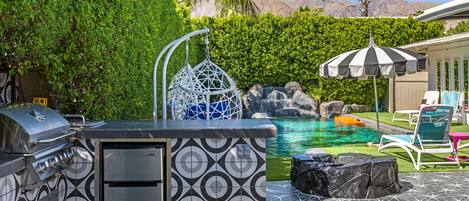 A backyard with a pool, a grill, and a hanging chair.