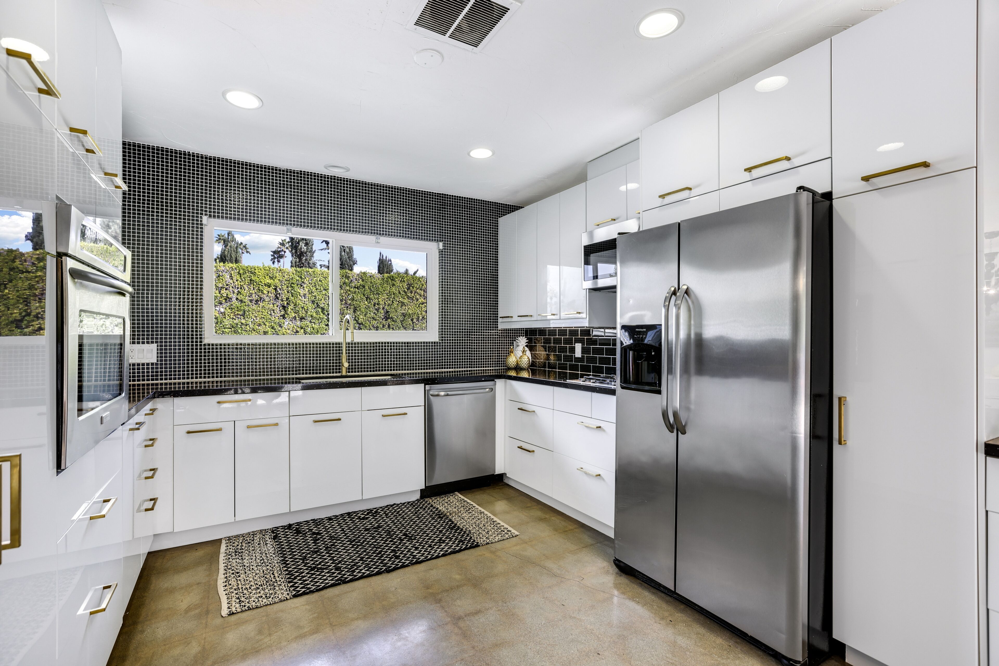 A modern kitchen with white cabinetry, a stainless steel refrigerator, and a black and white backsplash.