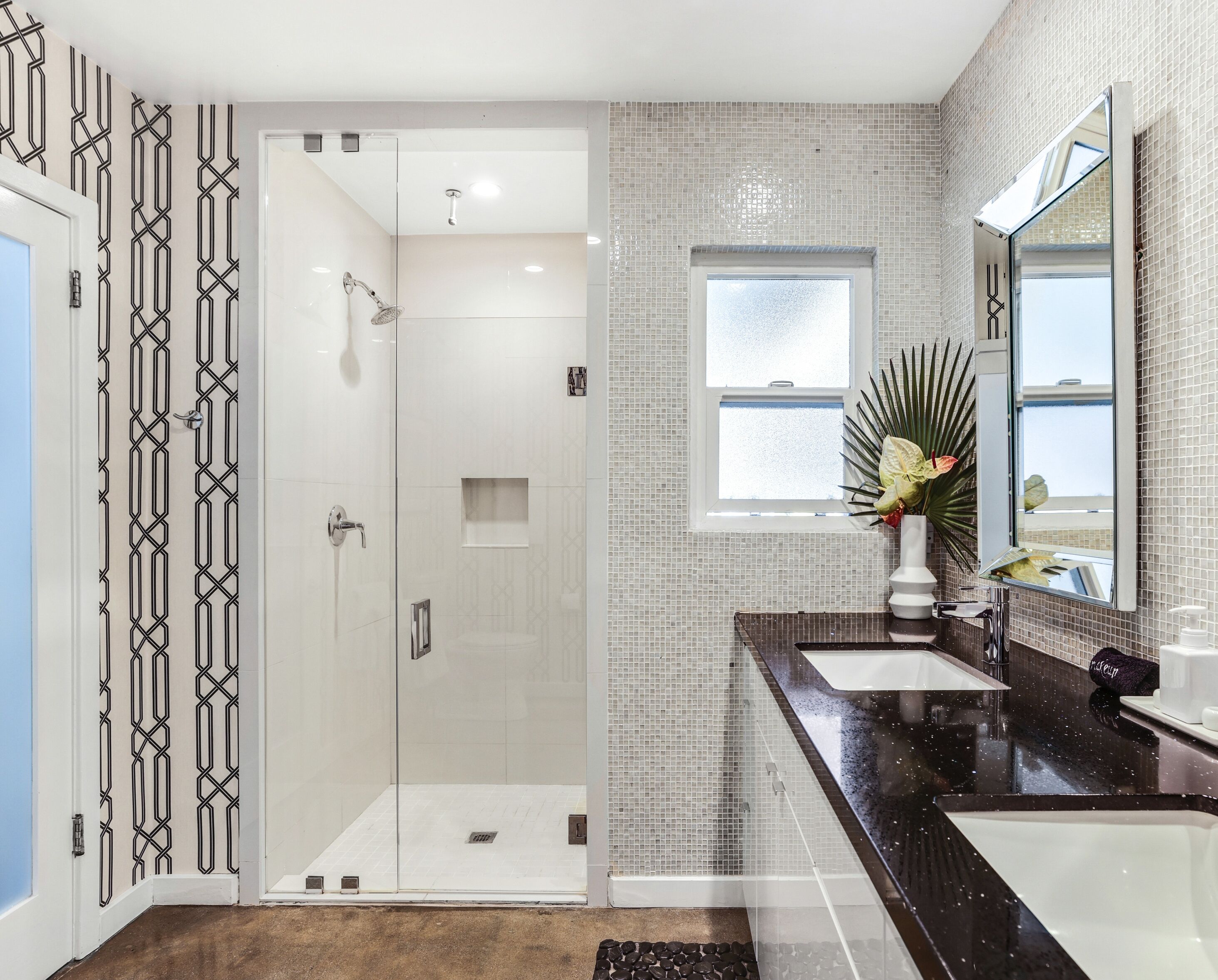 A modern bathroom with a walk-in shower, a large mirror, and a window providing natural light.