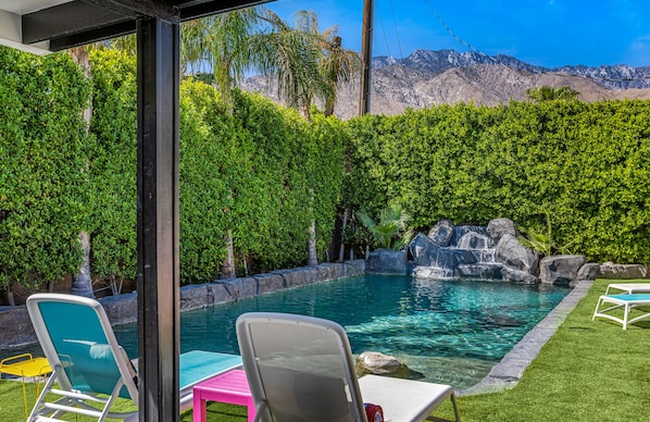 A backyard with a swimming pool, a waterfall feature, and a view of mountains.