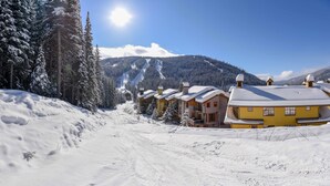 A snow-covered ski resort with multiple chalet-style buildings, a clear sky, and a mountain backdrop.