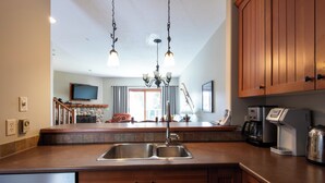 A kitchen with a double sink, wooden cabinets, a chandelier, and a television in the background.