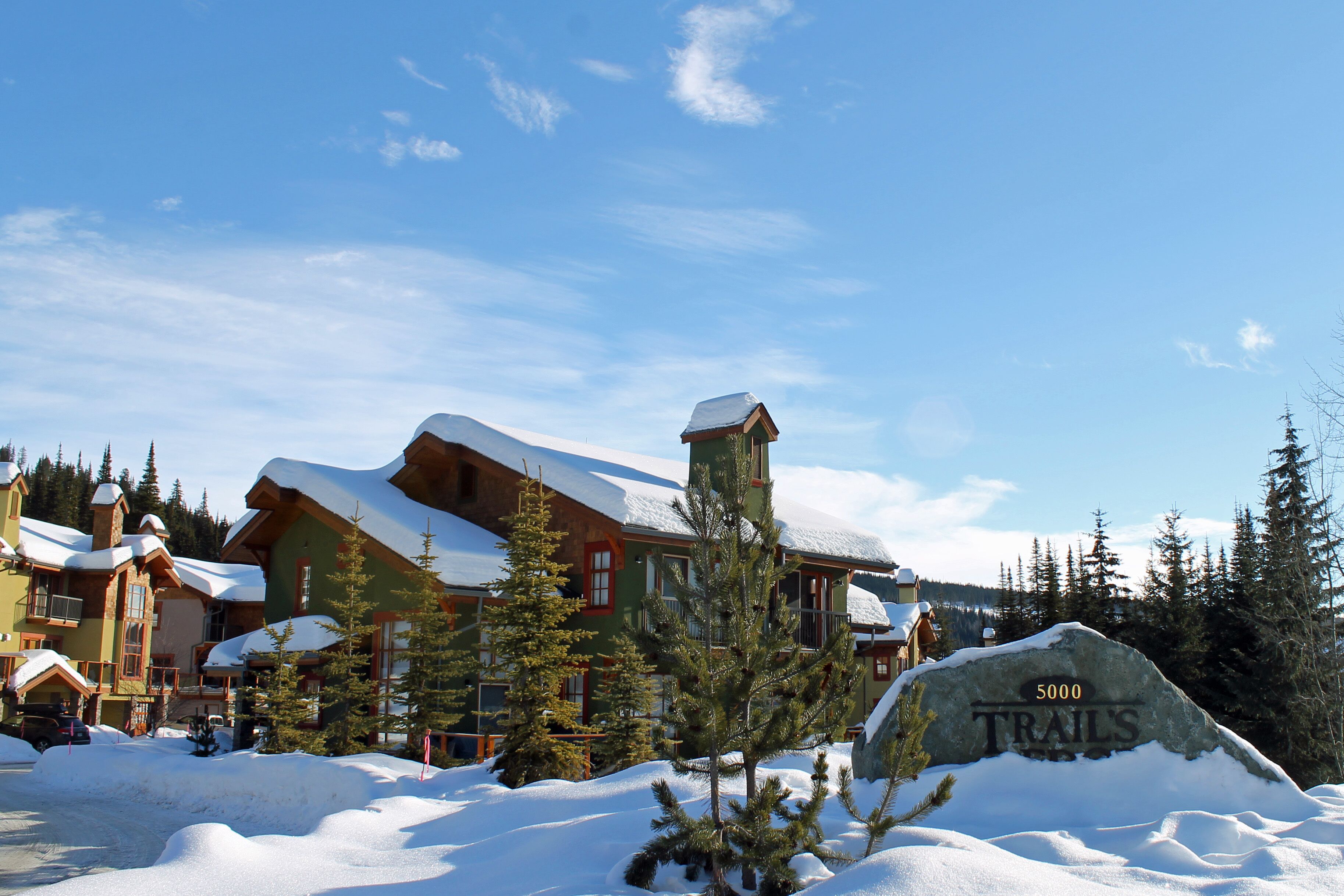 Un chalet enneigé, sur lequel on peut voir une grande enseigne en pierre indiquant « 5000 SENTIERS ».