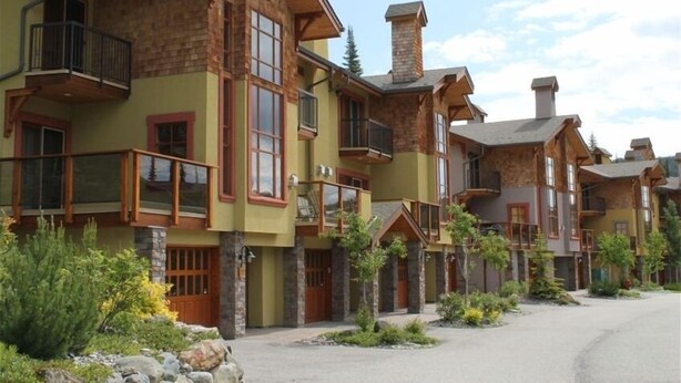 A row of multi-story buildings with balconies, large windows, and a stone facade.