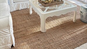 Un salón amplio con un sofá blanco, una mesa de centro de vidrio y un tapete tejido.