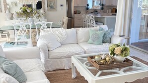 Un salón amplio con un juego de sofá blanco, una mesa de centro de cristal y objetos decorativos, además de una alfombra tejida.