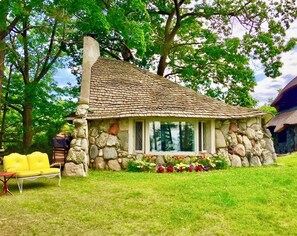 A stone cottage with a pitched roof, a window with a view, and a yellow chair outside.