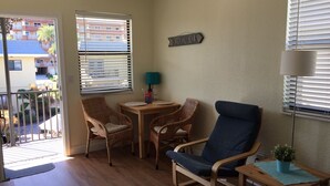A room with a balcony, wicker chairs, a blue armchair, a wooden table, and a lamp. - Adorable One Bedroom One Bathroom With Easy Access To The Beach!  (Redington Beach)