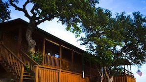 Une cabane en bois avec un mur de soutènement en pierre, un escalier en bois et un grand arbre en arri ère-plan.