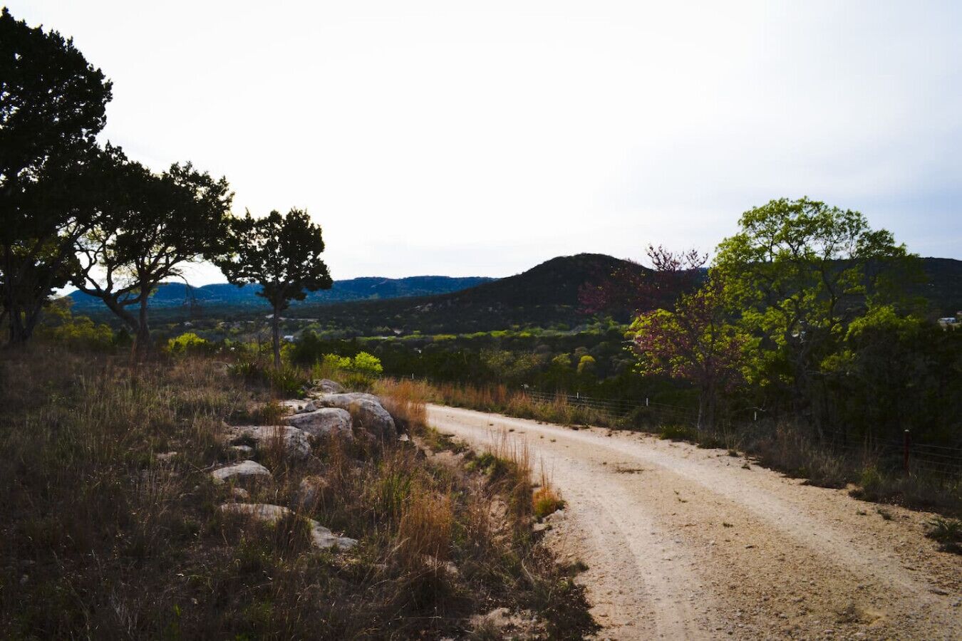 A dirt road winding through a natural landscape with sparse vegetation and distant hills.