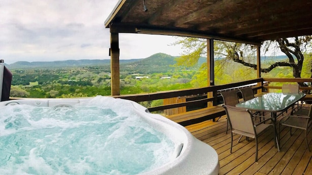 Un bain à remous sur une terrasse en bois, avec une table et des chaises, offrant une vue imprenable sur un paysage magnifique.