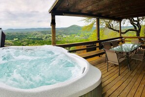Ein Whirlpool auf einer Holzterrasse mit Tisch und Stühlen, mit Blick auf eine reizvolle Landschaft.