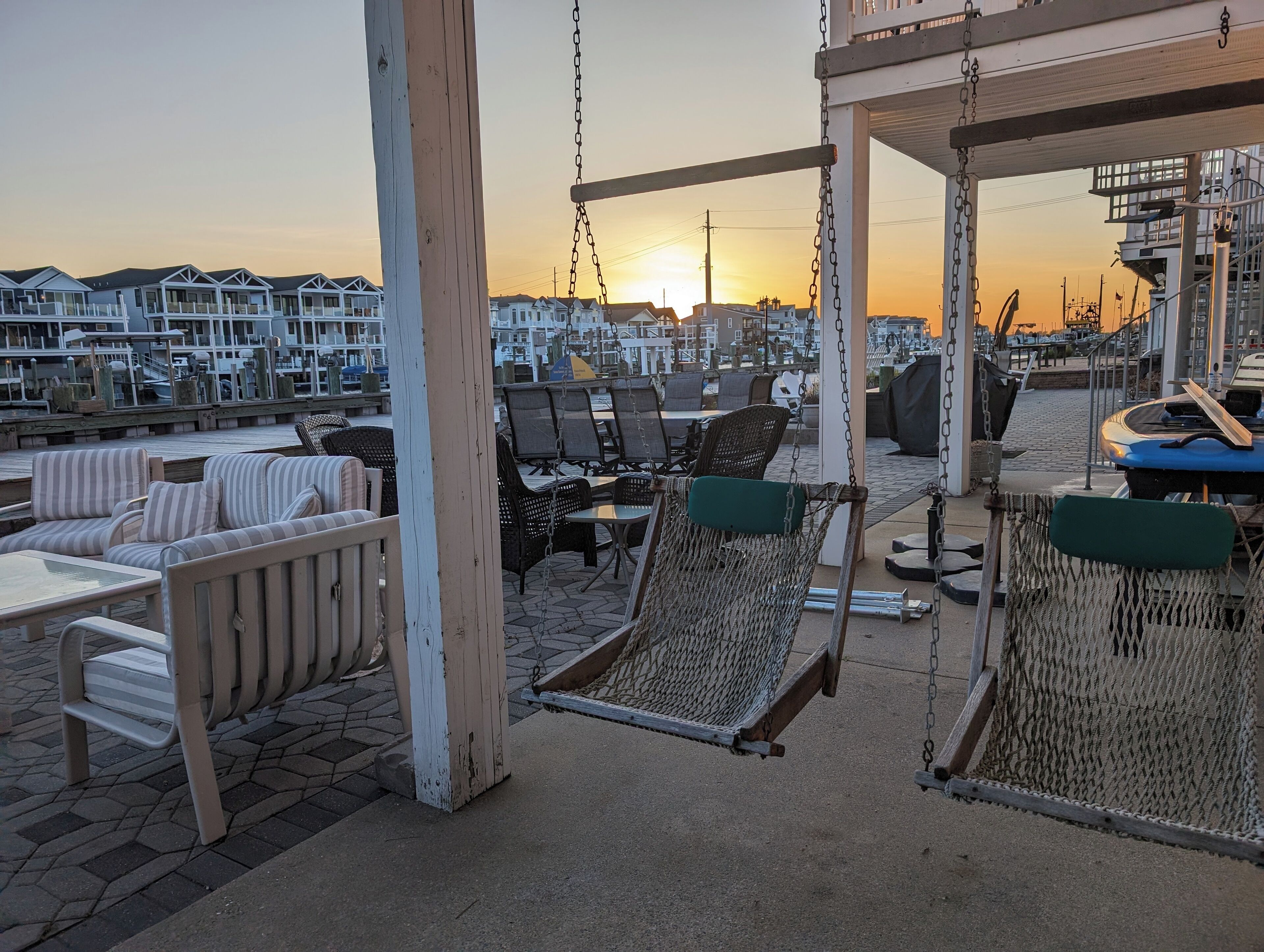 A seaside patio with wicker chairs and a hammock, overlooking a marina with boats and houses.