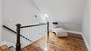 Un escalier avec une main courante en bois foncé et des balustrades blanches, menant à une mezzanine dotée d’un plancher en bois et d’un mur blanc.