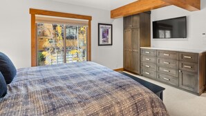 A bedroom with a large bed, wooden ceiling beams, a wardrobe, and a TV on the wall.
