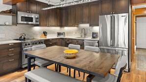 A modern kitchen with dark wooden cabinets, stainless steel appliances, a wooden dining table, and a bench.