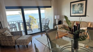 A room with a view of the sea, a sofa, a glass table, and a chair. - Coastal Bliss (Bradenton Beach)