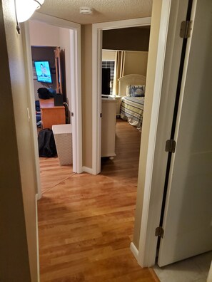 A hallway with a wooden floor leading to a bedroom with a bed and a nightstand. - Coastal Bliss (Bradenton Beach)