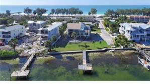 An aerial view of a coastal residential area with buildings, a dock, and a clear view of the ocean. - Coastal Bliss (Bradenton Beach)