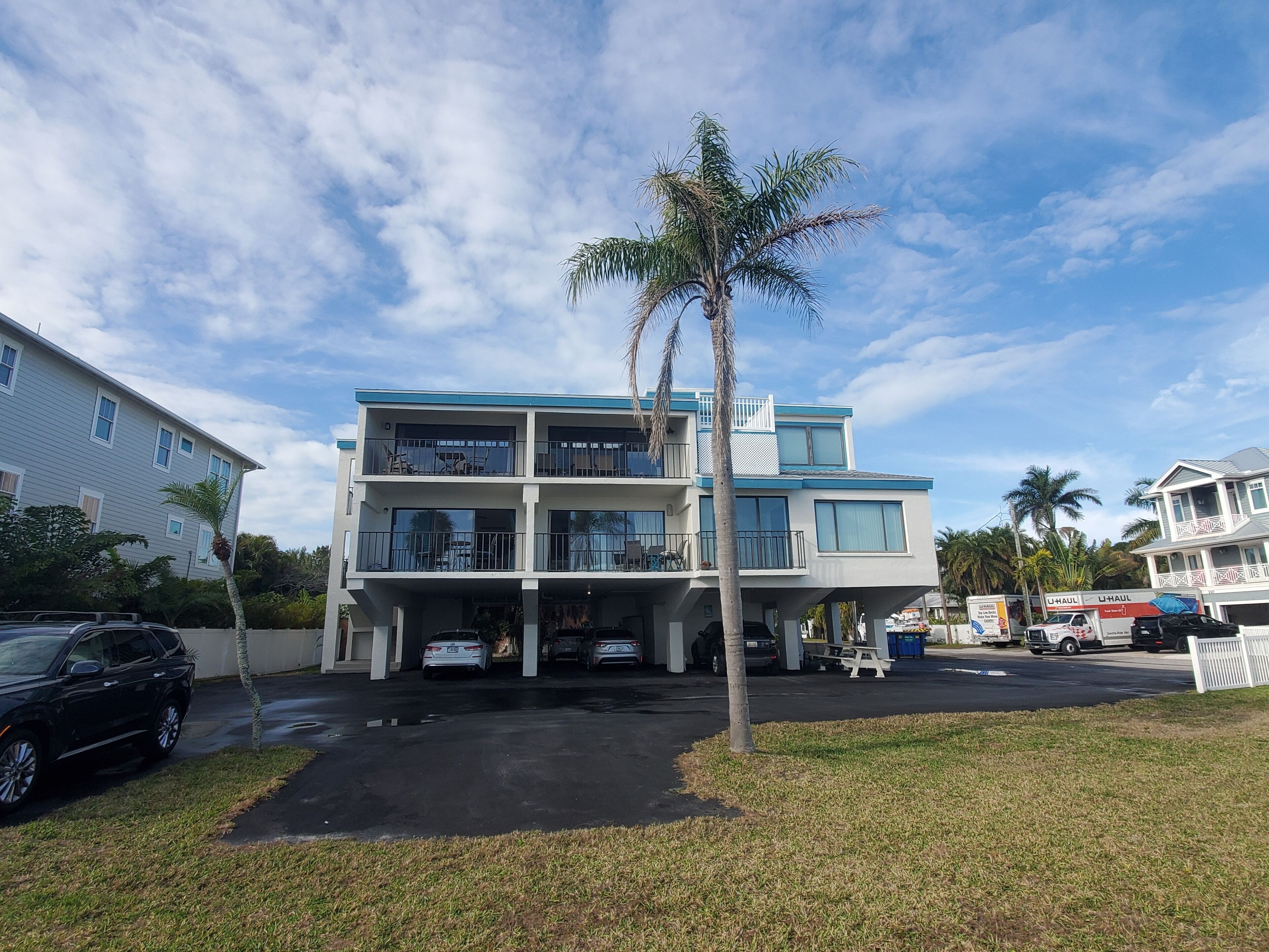 A two-story building with a balcony on the second floor, a parking area in front, and a palm tree nearby.