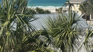 A view of a beach with palm trees in the foreground and a building with a red roof in the background. - Coastal Bliss (Bradenton Beach)