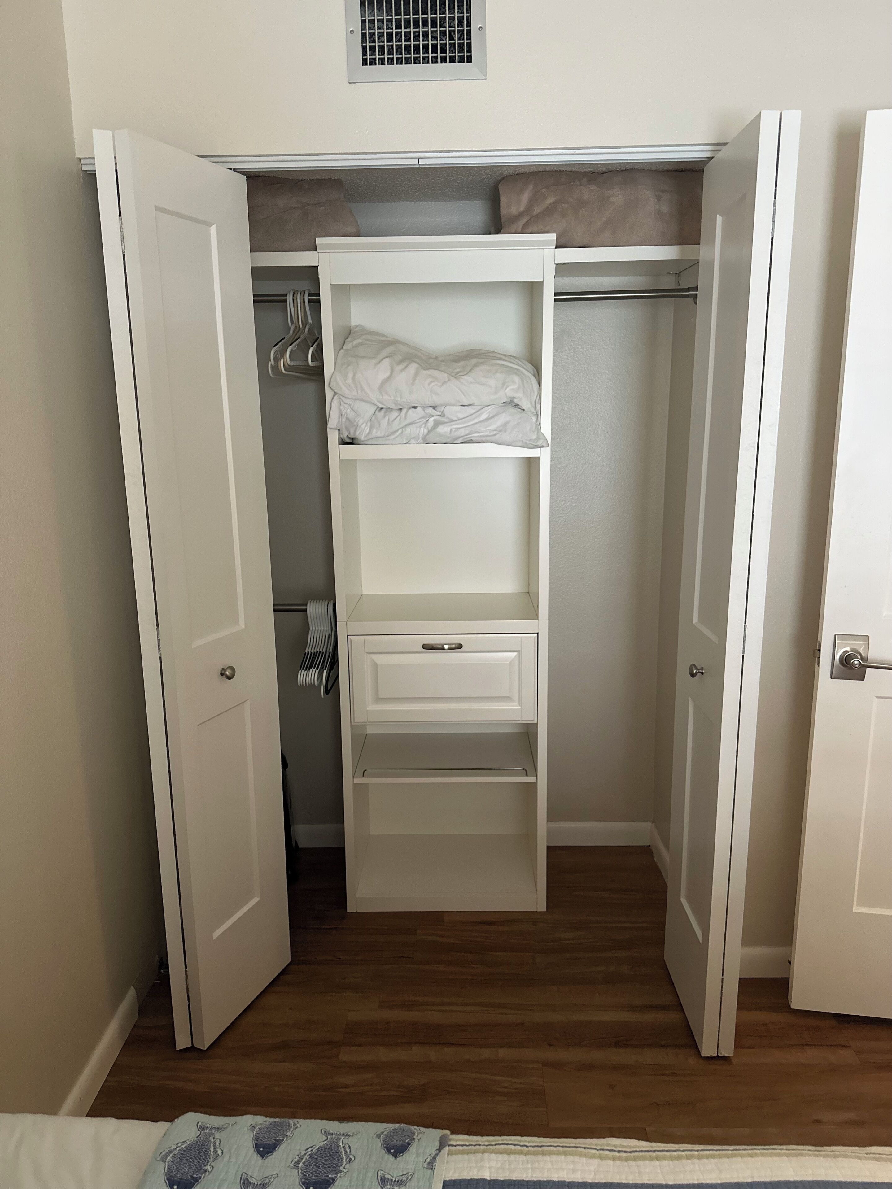 Een inloopkast met open deuren, een kledingroede en een uitgeschoven bed aan de bovenkant.