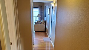 A hallway with wooden flooring leading to a living area with a sofa and a view of the outdoors. - Coastal Bliss (Bradenton Beach)