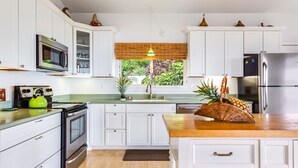 Una cocina moderna con armarios blancos, electrodomésticos de acero inoxidable, encimera de madera y vistas a zonas verdes.
