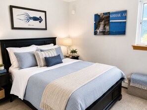 A neatly made bed with a blue and white bedspread, a framed picture of an arrow squid, and a wall-mounted sign with text. - Puffin Perch 3 Bed 2.5 Bath House & Save 10% on Rental Car in 2026 (Kodiak)