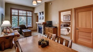A spacious living room with a fireplace, a dining area, and a bedroom with a large bed. - Capitol Peak Lodge 3123 (Snowmass Village)