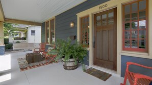 A covered porch with a wooden bench, a potted plant, and a red chair. - Classic 12 South Bungalow (Nashville)