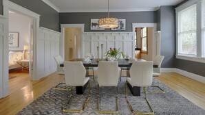 A dining room with a dark gray wall, white cabinetry, and a chandelier. - Classic 12 South Bungalow (Nashville)