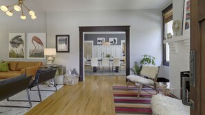A modern living room with a sofa, a coffee table, and a striped rug. There is a dining area with a table and chairs in the background. - Classic 12 South Bungalow (Nashville)