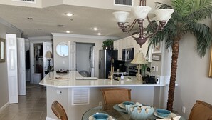 Una cocina moderna con una isla central, mesa de comedor con platos azules y una lámpara de araña.