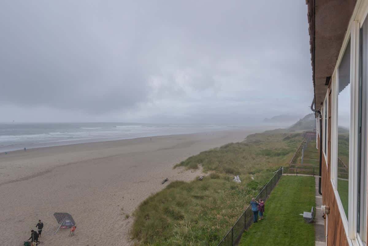 Een strand met een gazon en een gebouw met grote ramen met uitzicht op het strand.