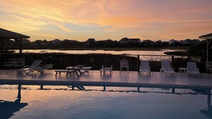 Zona junto a la piscina con sillones de descanso y vista a un lago al atardecer.