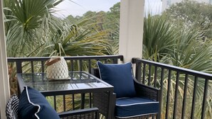 Un balcon agrémenté de fauteuils en osier et d’une table en verre, entouré d’une végétation luxuriante.