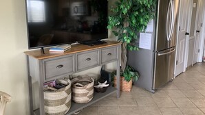 Une cuisine équipée d’un grand téléviseur à écran plat posé sur un meuble en bois, d’un réfrigérateur et d’une plante en pot.