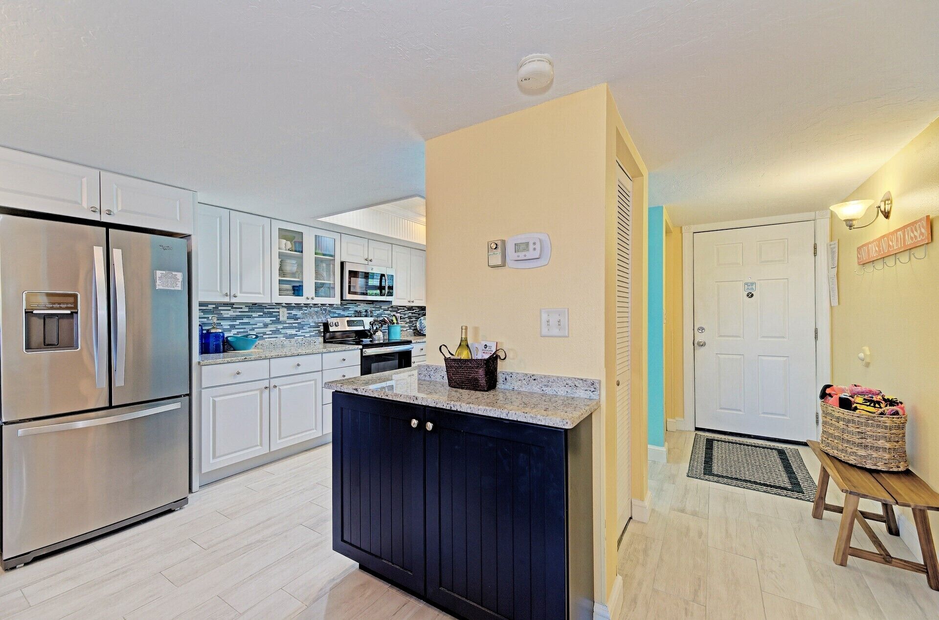 A modern kitchen with stainless steel appliances, a central island, and a hallway leading to a door.