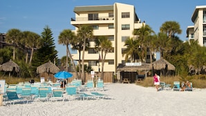 Ein Strandhotel mit mehreren Balkonen, Palmen und Liegestühlen.