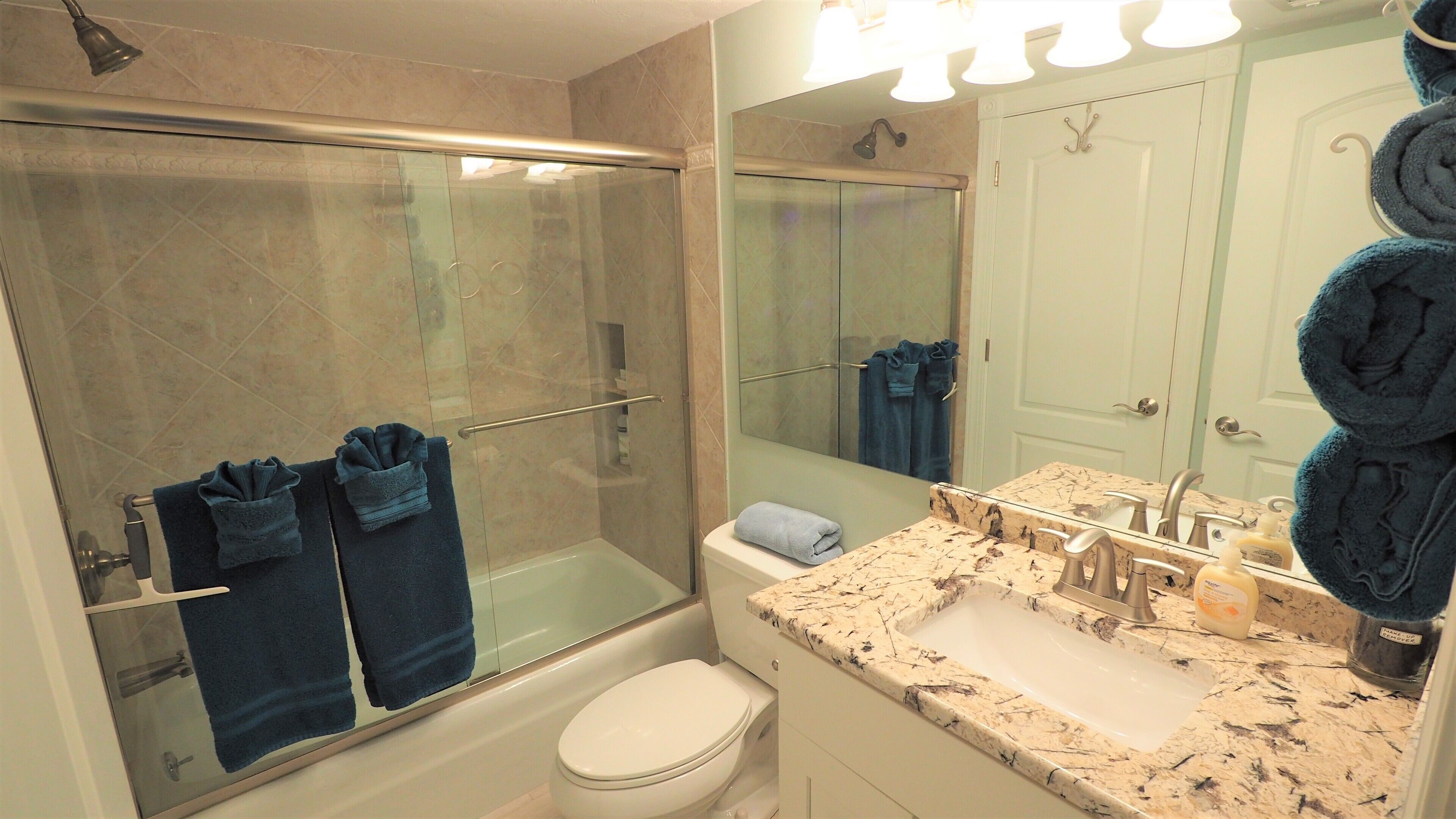 Une salle de bain moderne avec une douche à parois de verre, des toilettes blanches, un lavabo en marbre et un grand miroir.