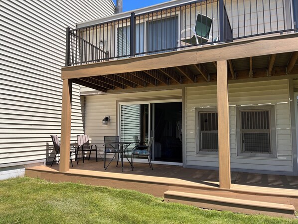 A covered outdoor deck with a table and chairs, a sliding glass door, and a window with blinds.