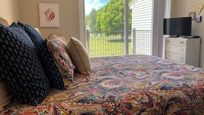 A bedroom with a large bed, a television, and a view of a green lawn through a sliding door. - Cozy and Convenient! (Cedar)